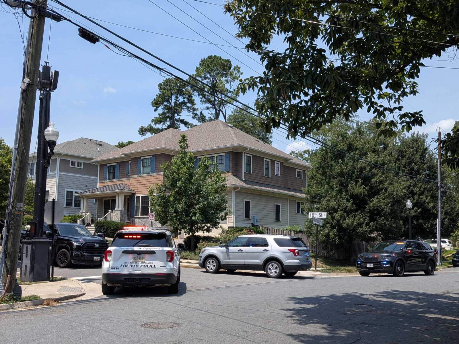Residential intersection with police cars parked on the street; county police vehicles visible by the curb and a street sign reads 18th St N.