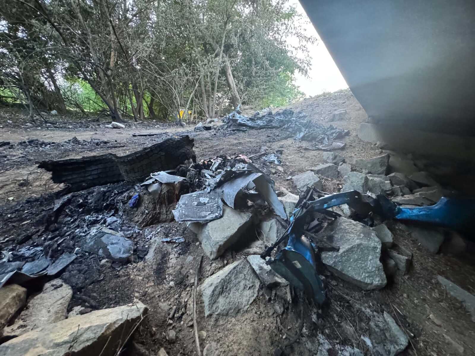 Rubble and charred debris scattered on dirt ground near trees, with a large burnt log in the foreground.