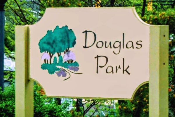 Sign reading 'Douglas Park' with a stylized tree illustration in teal and purple, set among greenery.