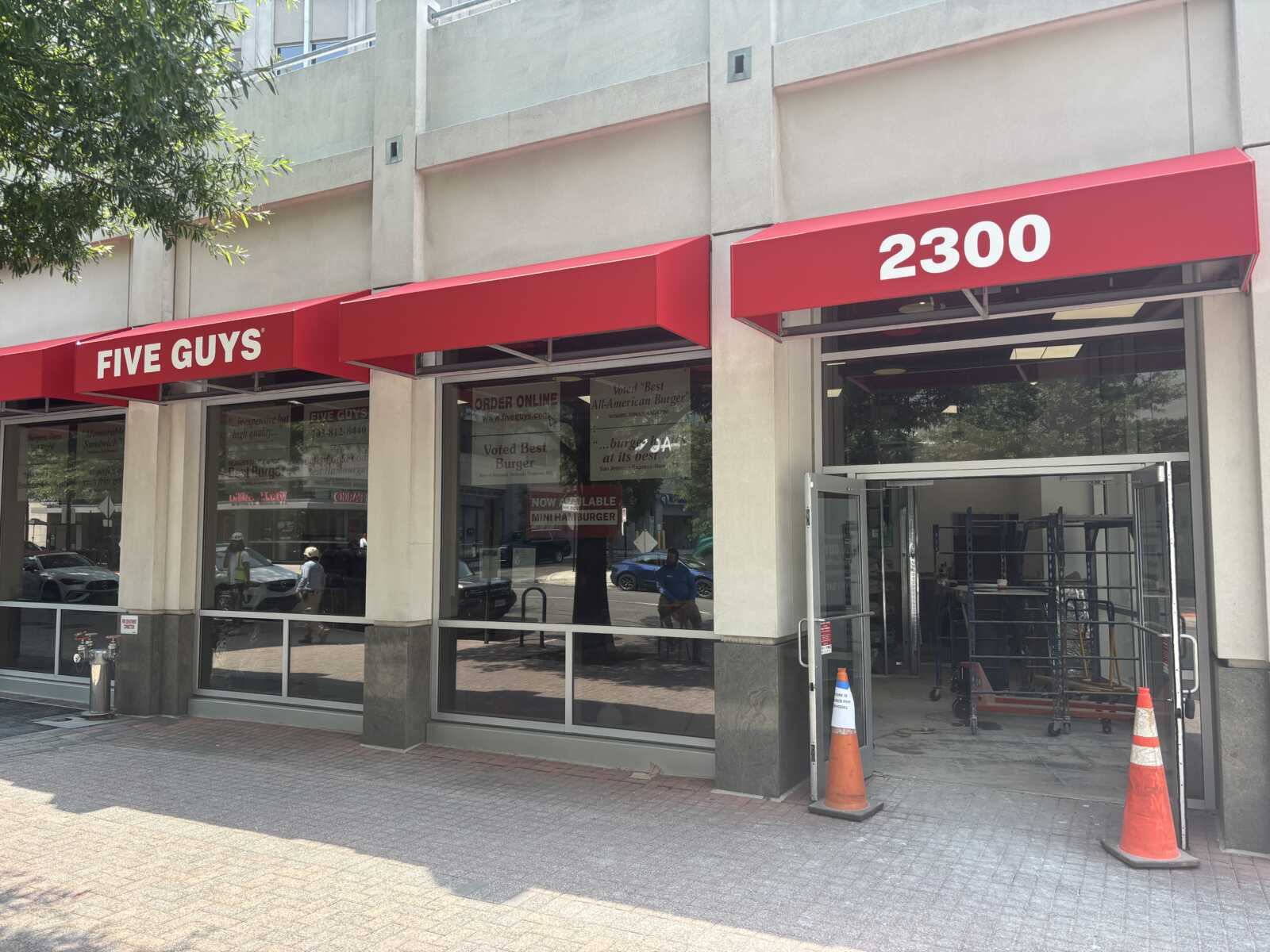 Exterior view of a Five Guys restaurant with red awnings reading 'FIVE GUYS' and the number '2300' above the entrance.