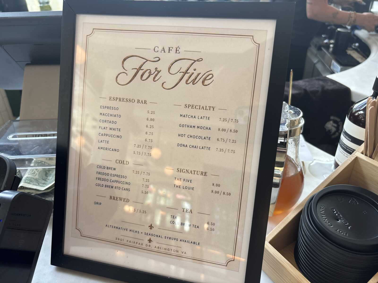 Framed cafe menu titled 'Cafe For Five' on a counter, listing espresso and specialty drinks.
