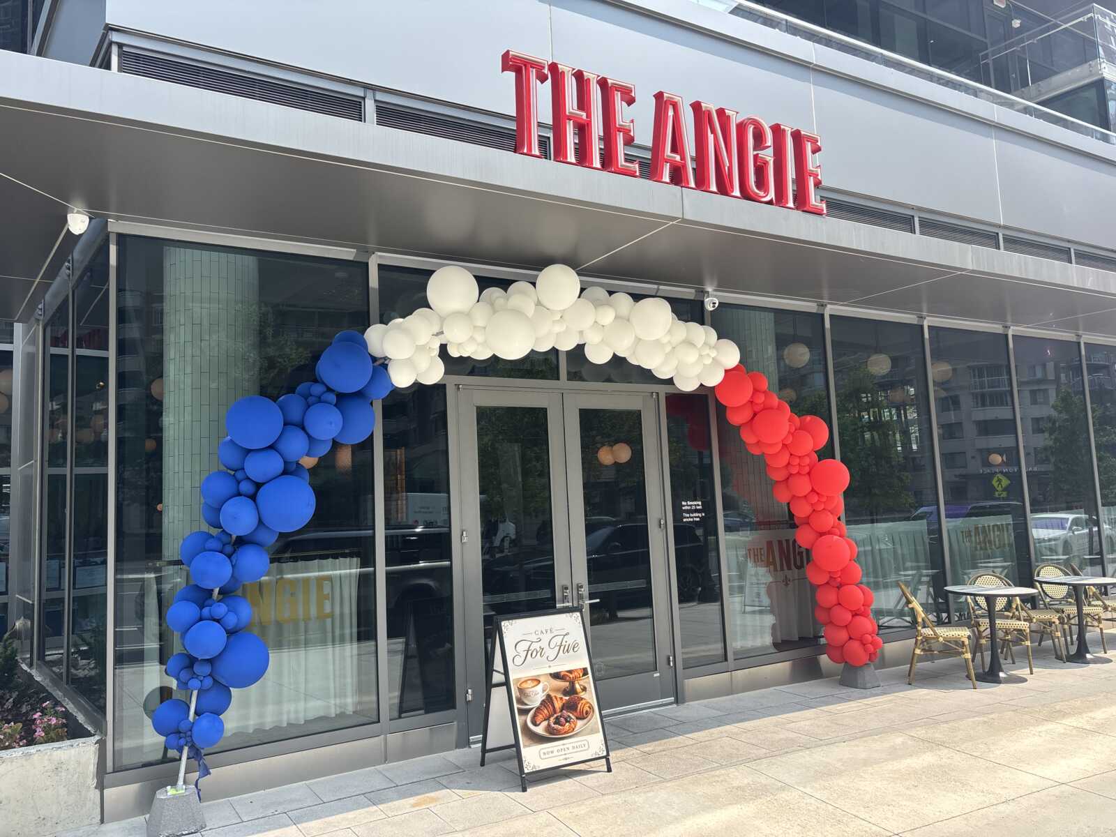 Storefront with a red THE ANGIE sign and a large balloon arch in blue, white, and red outside the entrance, suggesting a grand opening or celebration.