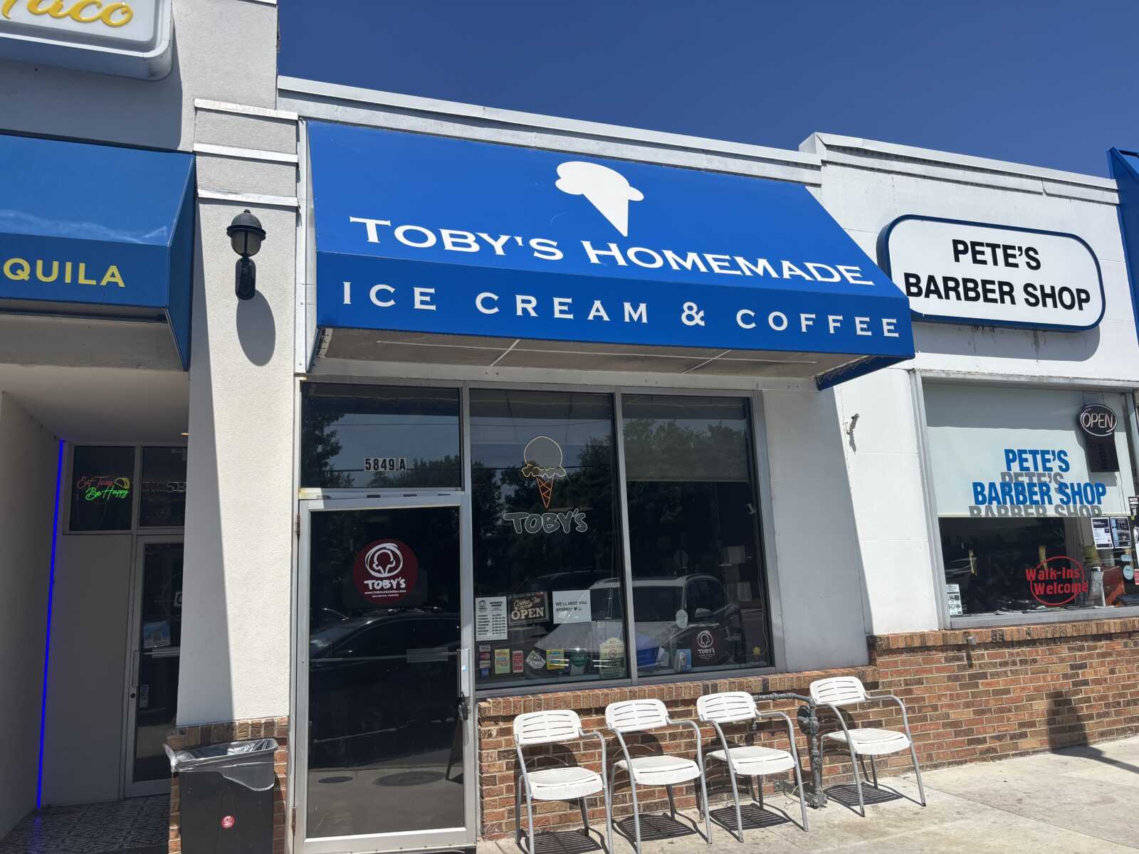 Front of Toby's Homemade Ice Cream & Coffee shop with a blue awning and glass doors, white chairs outside on the sidewalk.