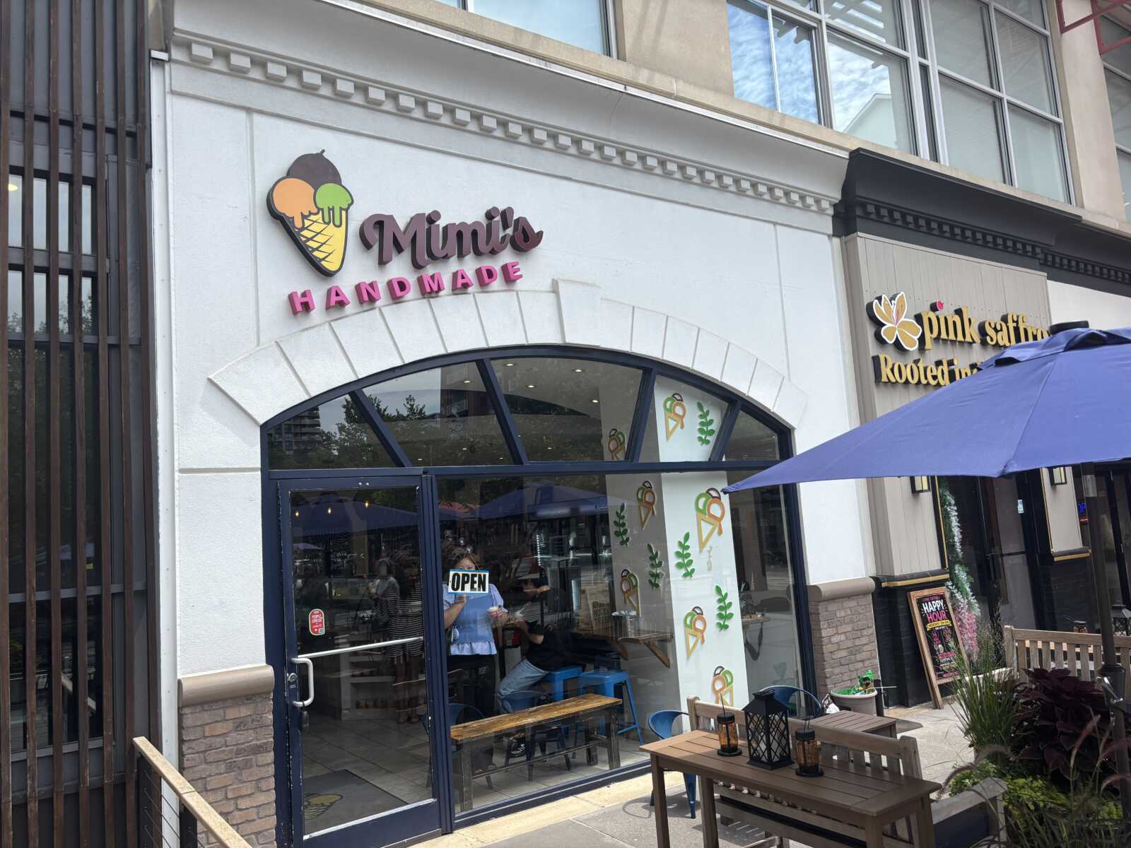 Storefront sign reading Mimi's Handmade with ice-cream cone logo; outdoor seating under blue umbrella outside the shop