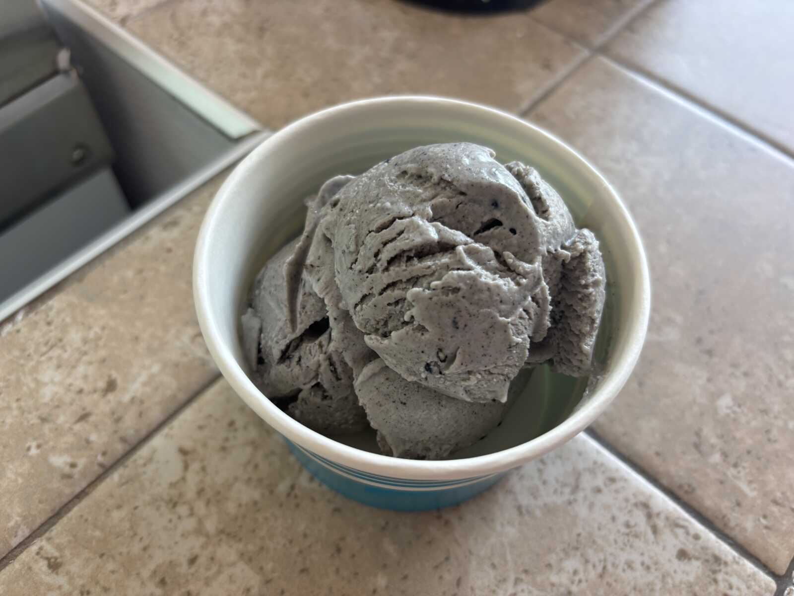 Cup of gray ice cream scoops in a small blue-rimmed cup on a tiled counter