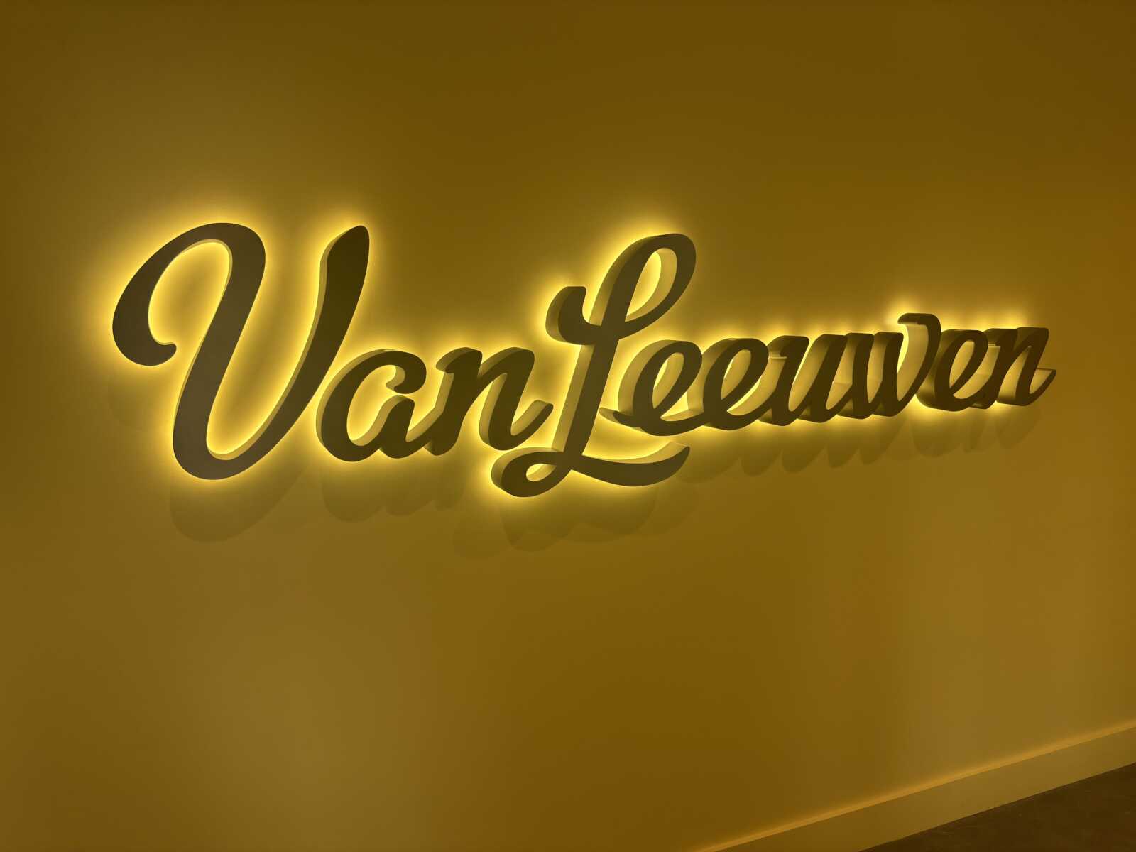 Yellow wall featuring a glowing neon-style cursive sign that reads 'VanLeeuwen'.