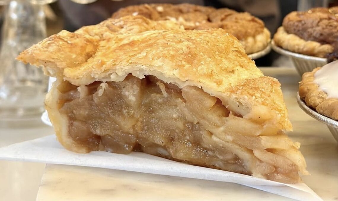 Slice of apple pie with a flaky golden crust and warm apple filling on a parchment-lined surface