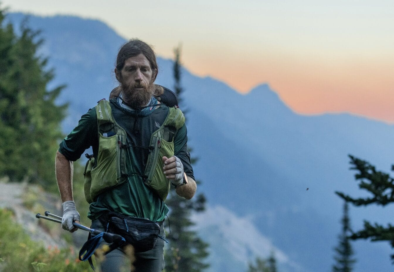 Mike Wardian running The Pacific Crest Trail (via mikewardian/Instagram) | ARLnow Hiker with trekking poles on a mountain trail at sunset, wearing a green vest and backpack.