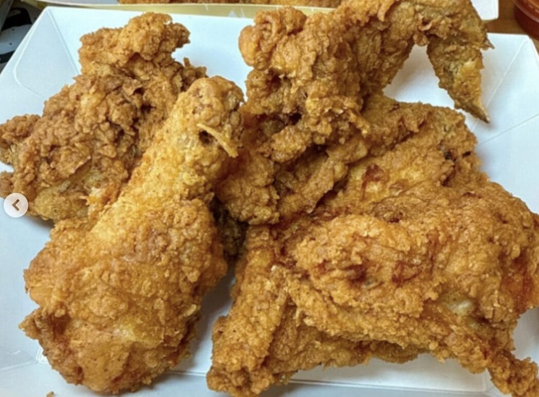 Several pieces of crispy fried chicken piled on a white takeout tray