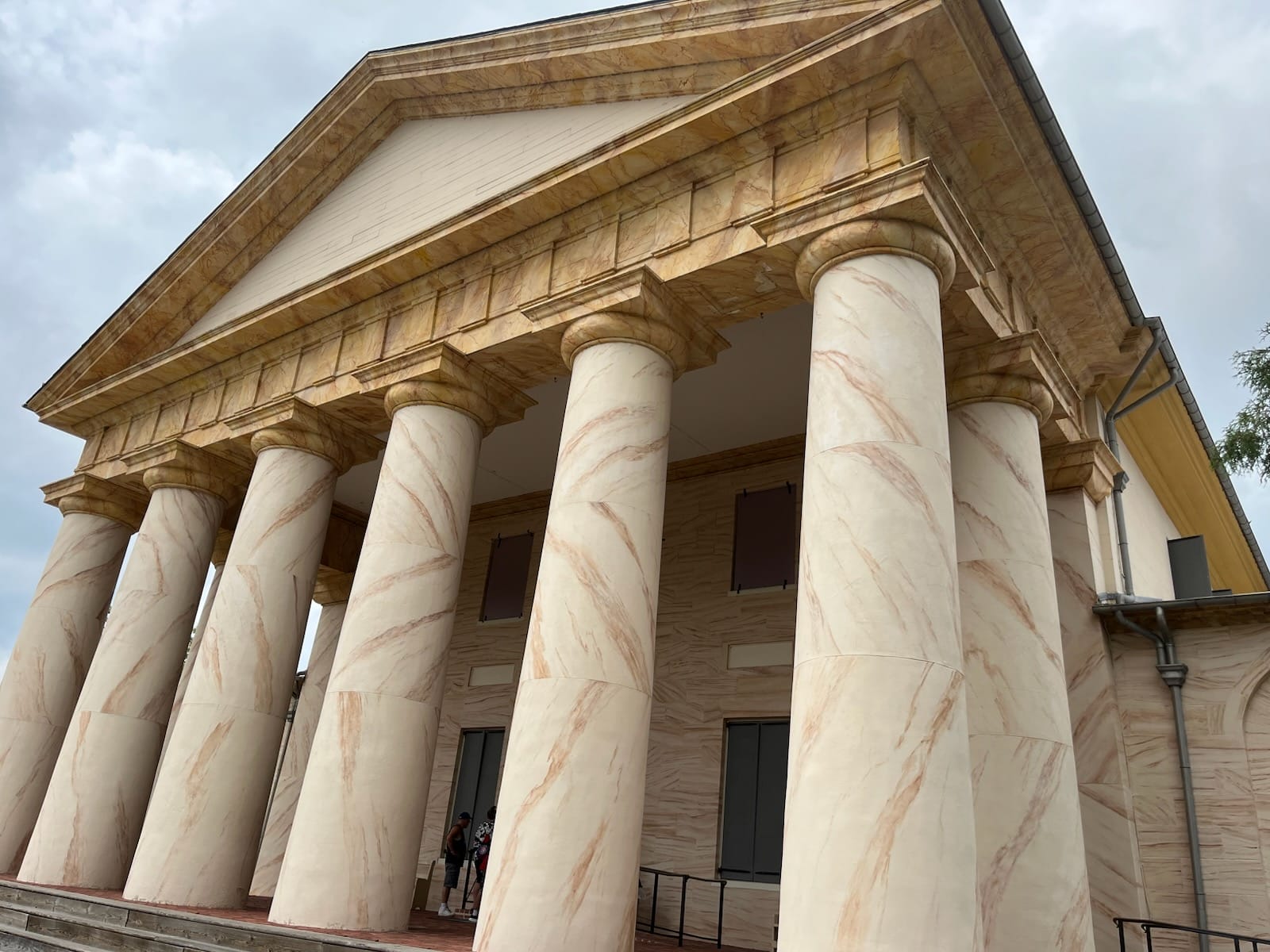 Classical marble building with tall round columns and a triangular pediment under a cloudy sky