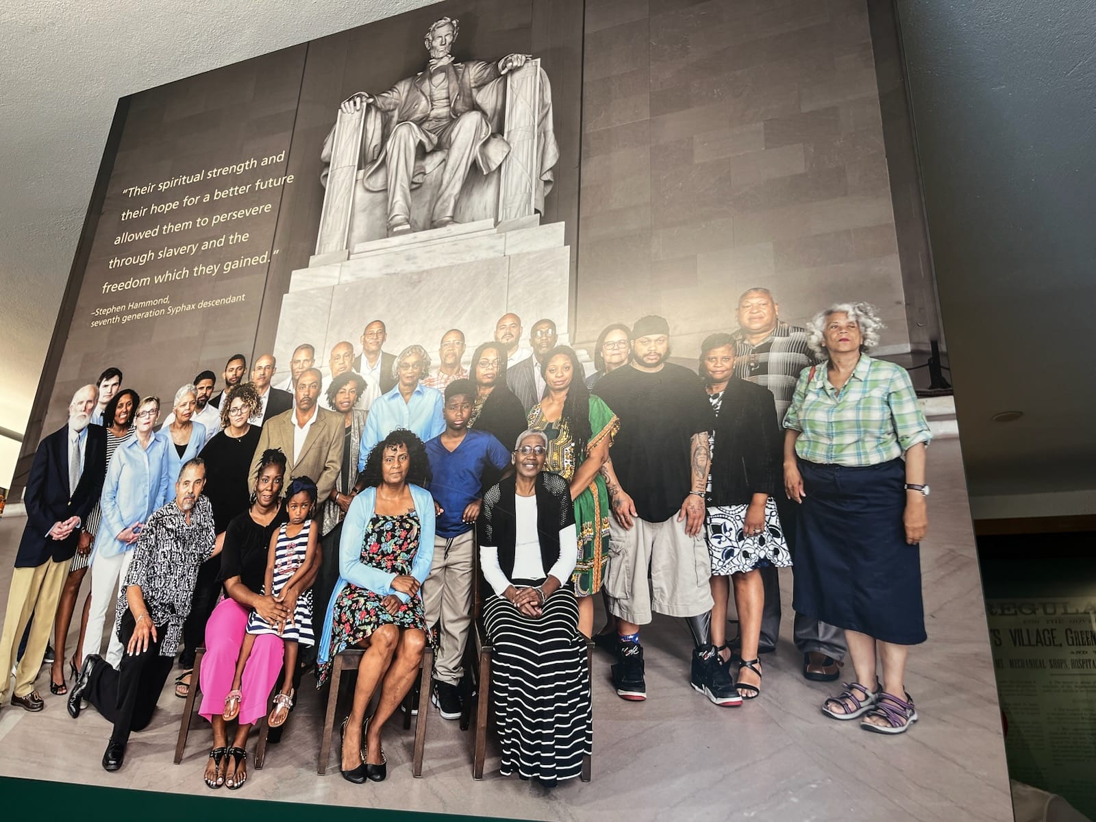 Diverse group of people posing for a group photo in front of a large statue panel with a quote on the left wall.