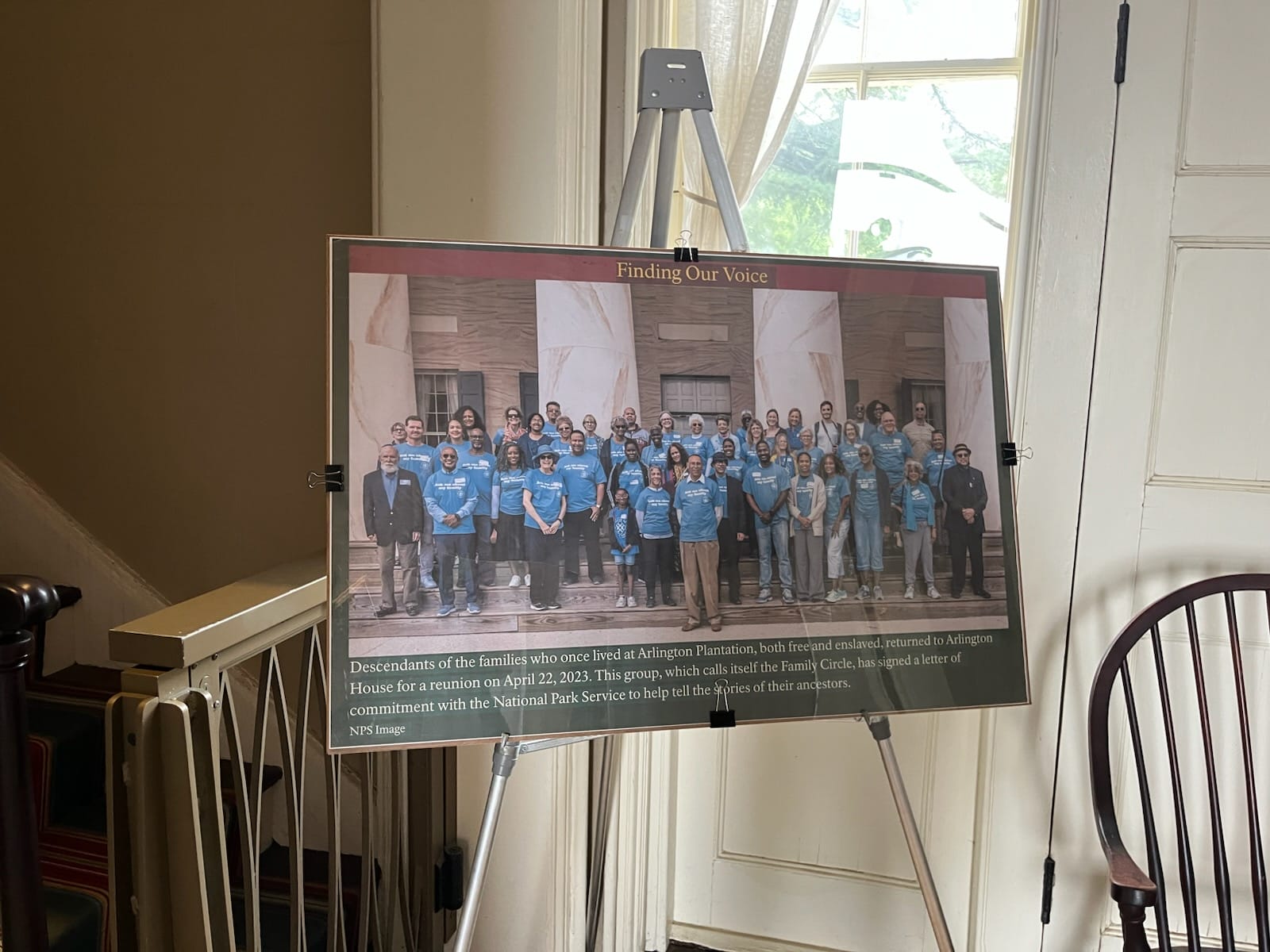 Framed group photo of diverse people in blue shirts posing on steps under a banner that says Finding Our Voice.