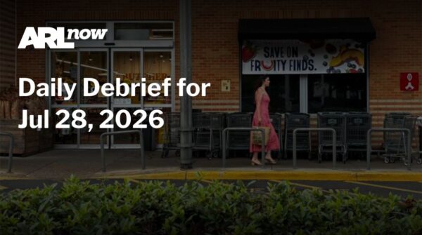 Overlay text reads 'Daily Debrief for Jul 28, 2026' on a dark storefront background; a woman in a pink dress walks past shopping carts outside a grocery store.
