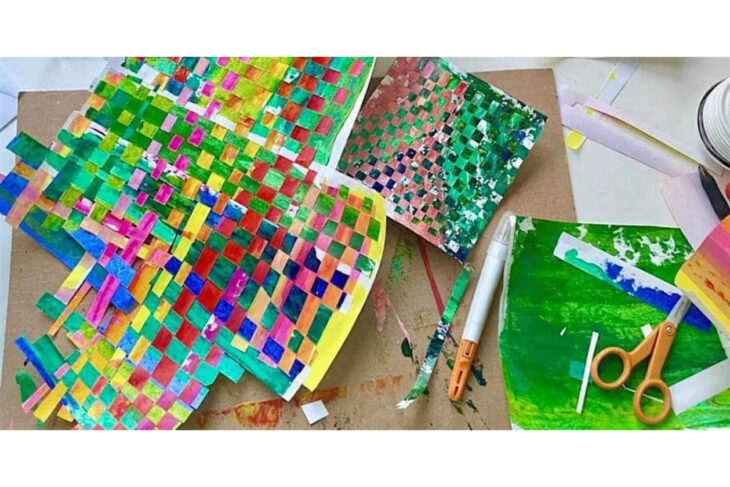 Colorful mosaic artwork made of small square paper pieces on a craft table with scissors and glue nearby.
