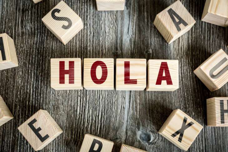 Wooden letter blocks spell HOLA on a dark wooden surface, forming a greeting in Spanish.