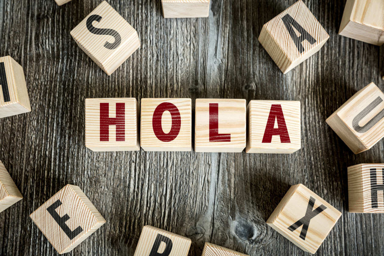 Wooden letter blocks spell HOLA on a dark wooden surface, forming a greeting in Spanish.