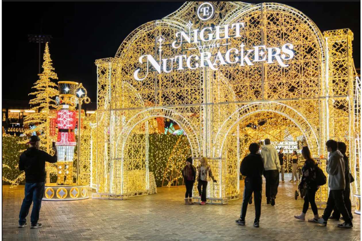 Golden, intricate illuminated arches form an entrance with the sign 'Night of the Nutcrackers' as visitors walk through at night.