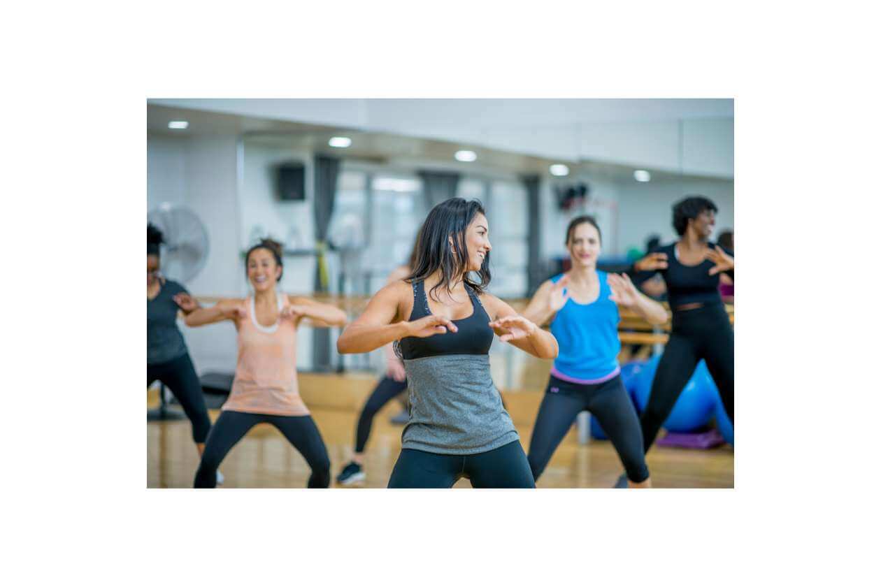 Group fitness class in a studio with women dancing energetically in coordinated moves.