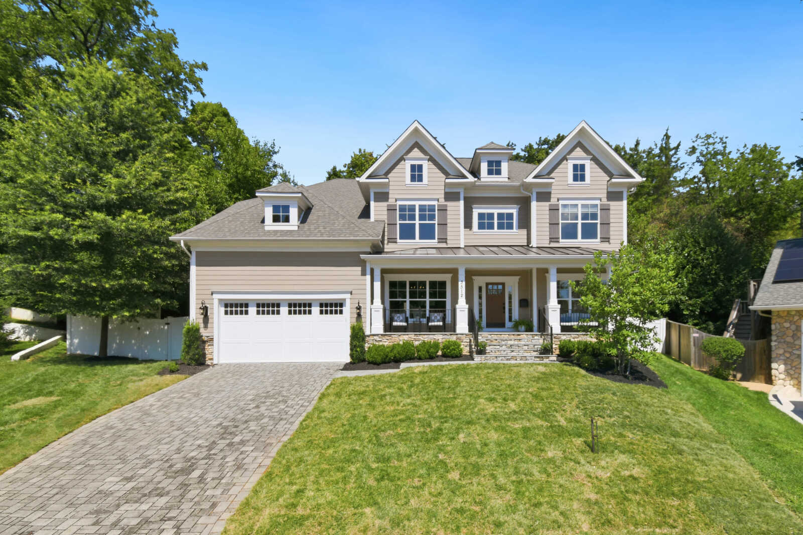 Front view of a beige two-story family home with a two-car garage, stone accents, and a covered front porch under a blue sky.