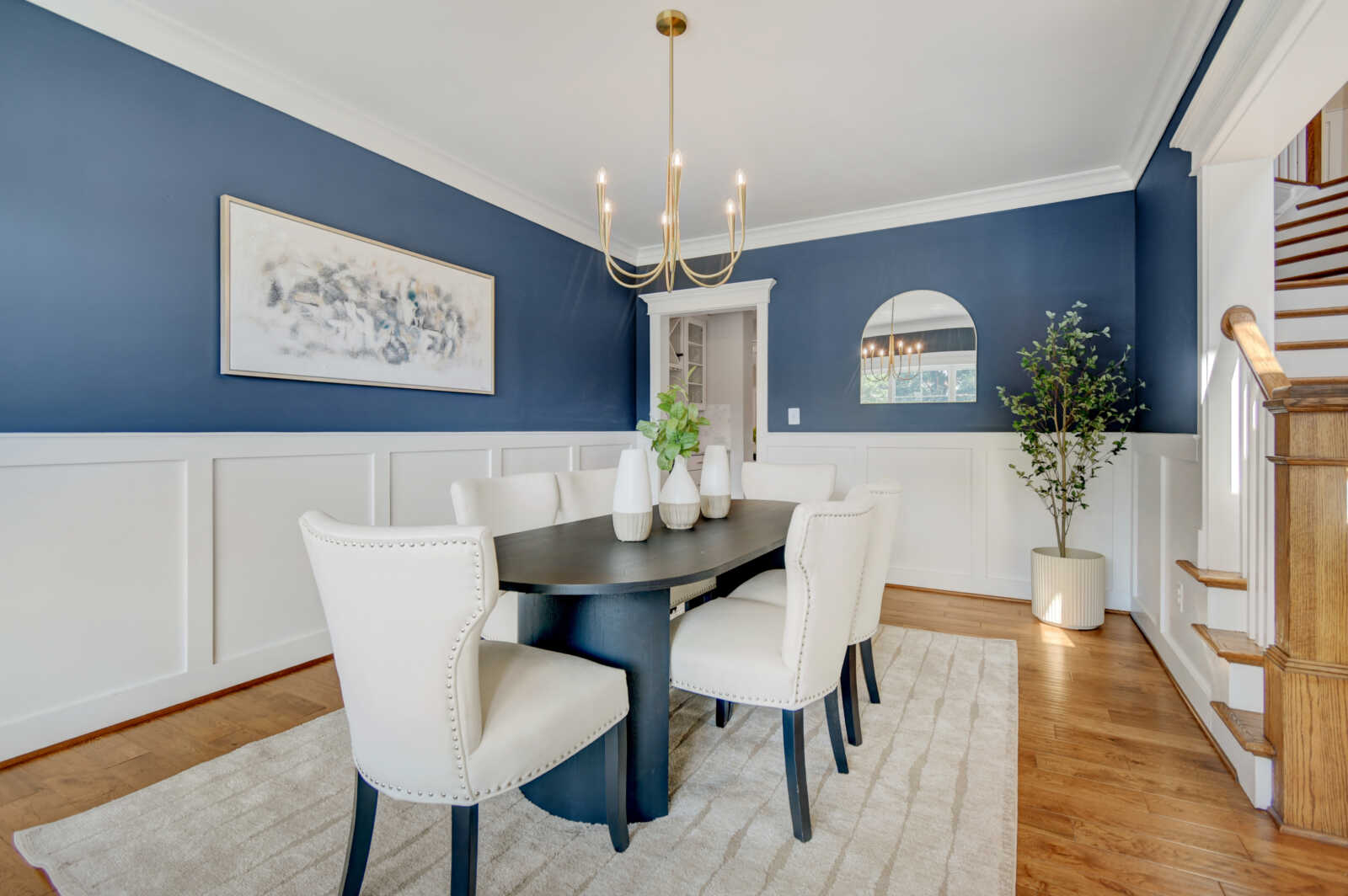 Dining room with navy walls and white wainscoting, featuring a dark rectangular table and six white upholstered chairs.