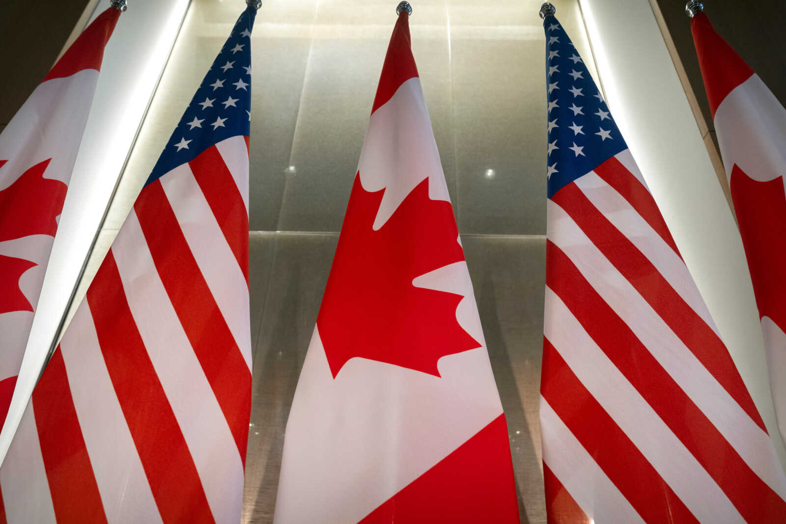 Flags of Canada and the United States displayed together in a row, center Canadian flag with red and white, flanked by US flags with stars and stripes.