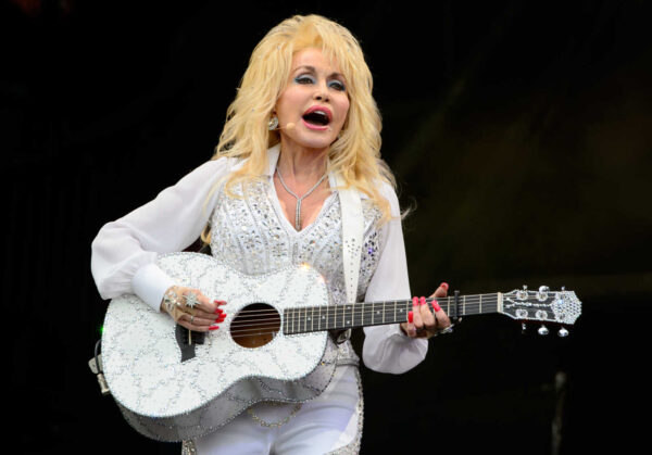 Female country singer in a sparkling white outfit, strumming a glittery white guitar on stage and singing into a headset mic.