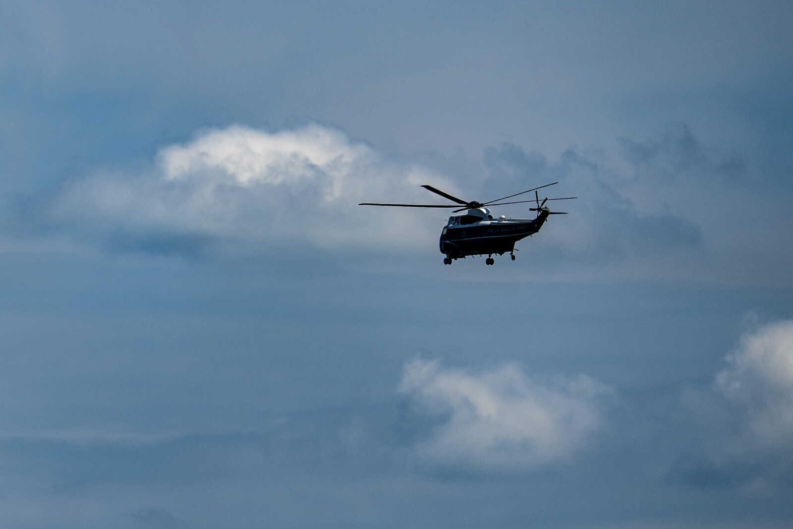 Medium-sized dark blue helicopter in flight against a cloudy blue sky, side view.