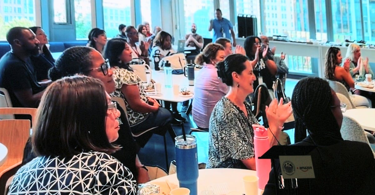 Diverse group of professionals clapping at a workshop or conference in a bright room with large windows.