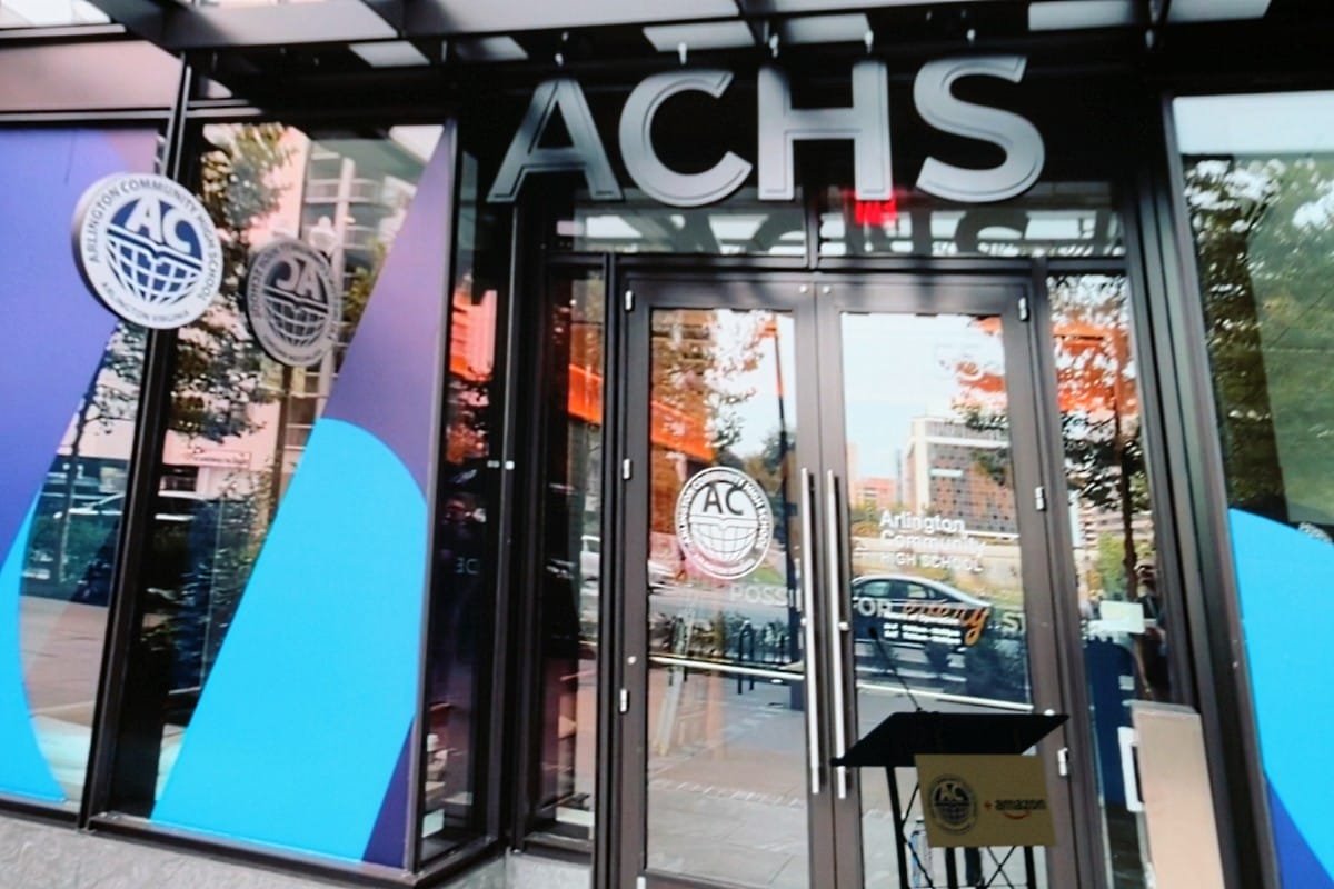 Entrance to an ACHS building with glass doors and large white ACHS letters above the entry.(center-right shows a podium)