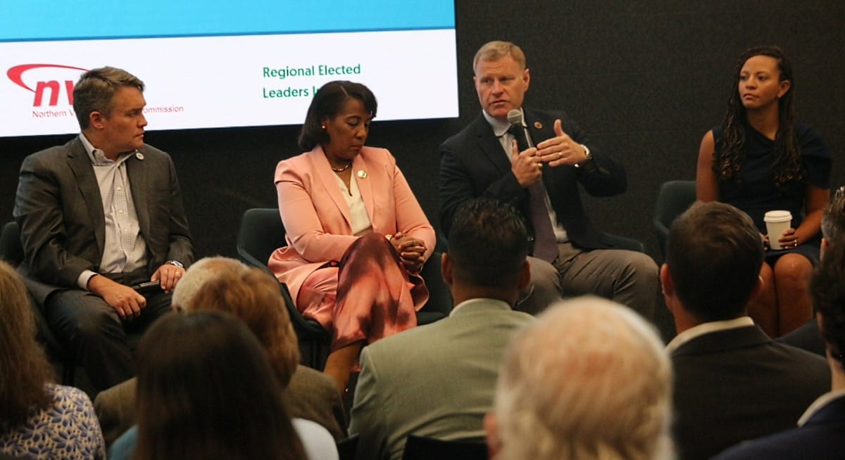 Panel discussion with four speakers on stage at a conference, one man speaking into a microphone as others listen.
