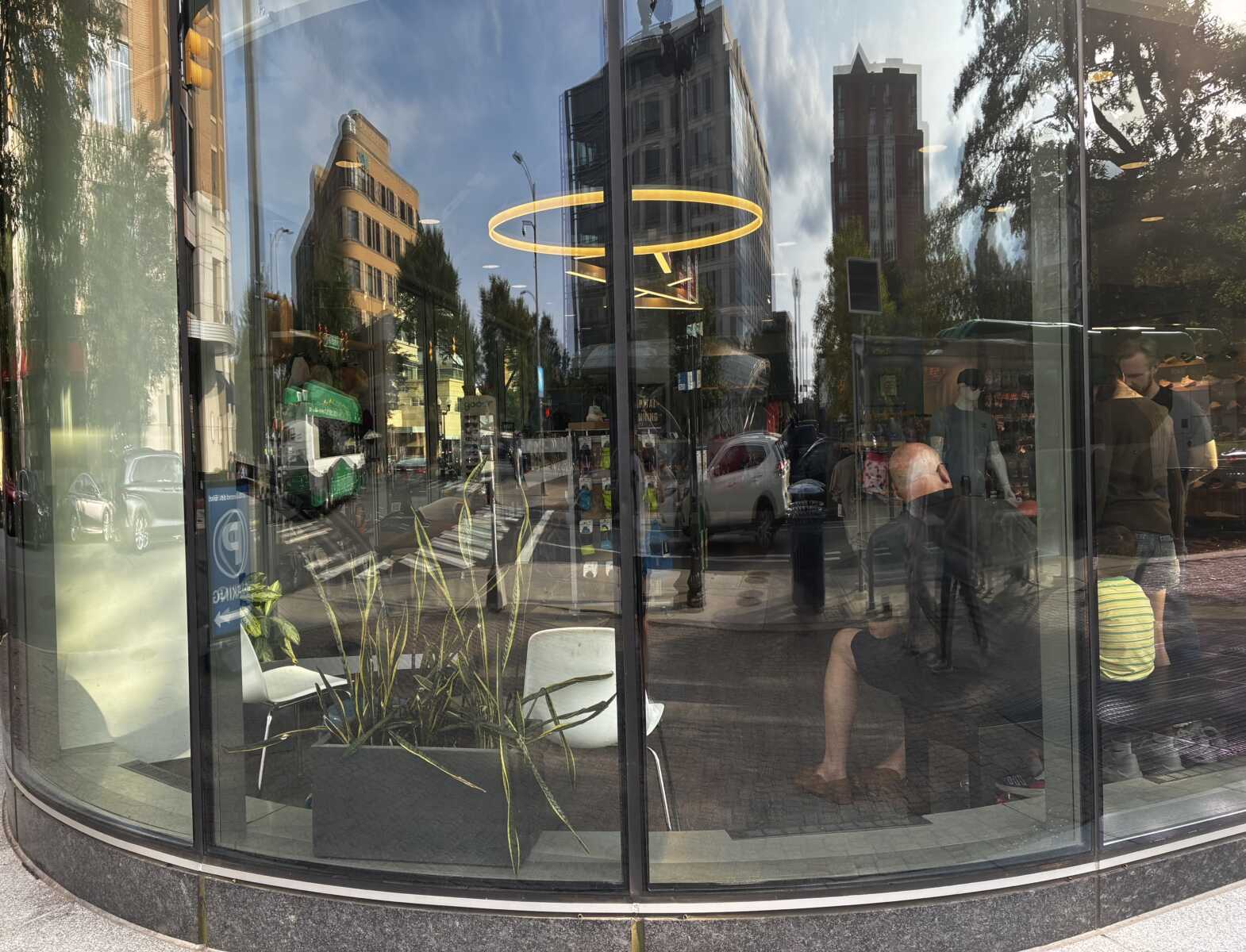 Clarendon skyline reflected in Pacers Running windows (courtesy George Brazier) | ARLnow Storefront glass window reflecting a city street, with a bright circular yellow light and interior mannequins visible inside.
