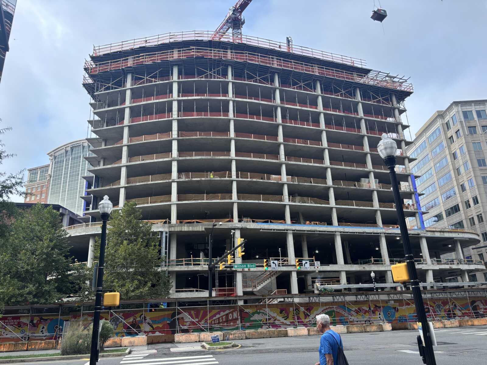 Under-construction high-rise with exposed concrete floors, scaffolding, and a crane overhead in a city setting
