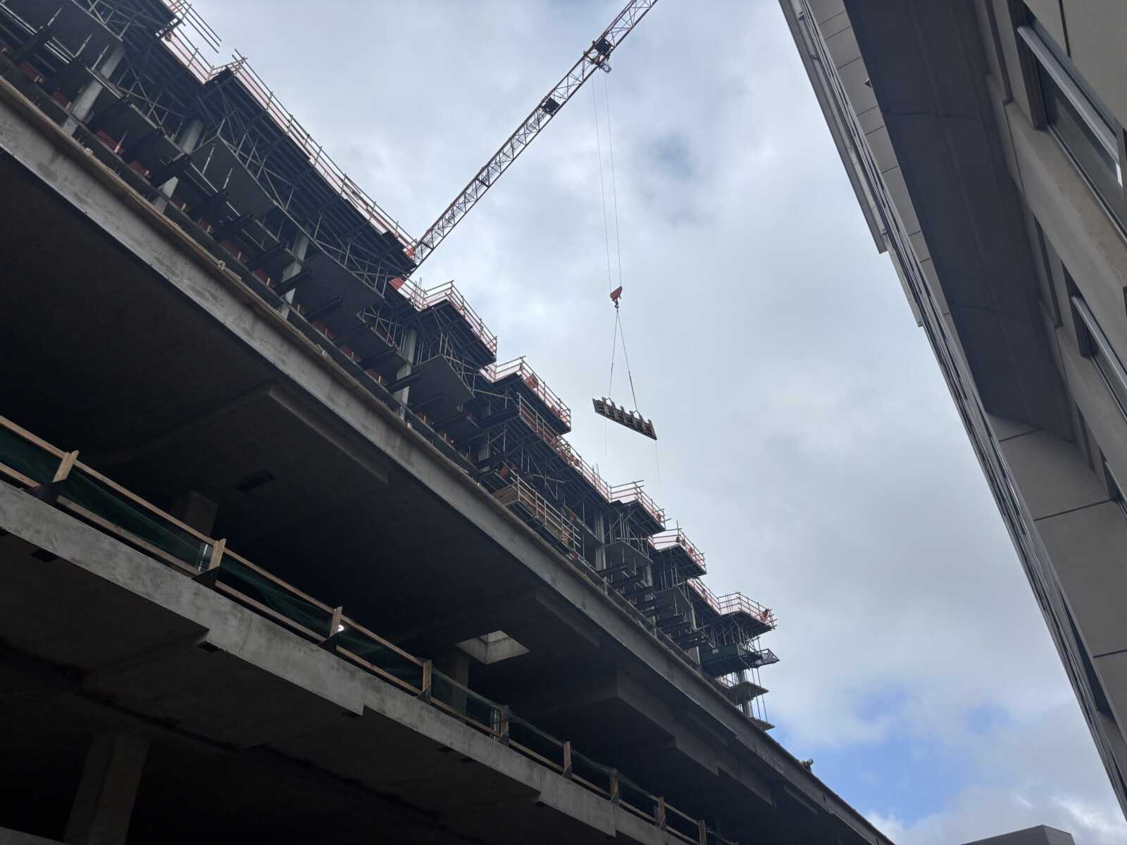 Crane lifts a beam over a multi-story construction site with scaffolding and concrete floors.