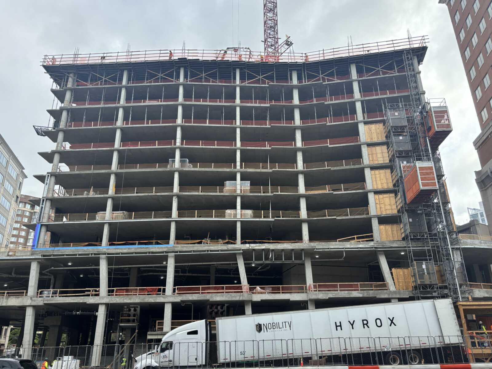 Under-construction multi-story concrete building with a crane overhead and workers on the top level.