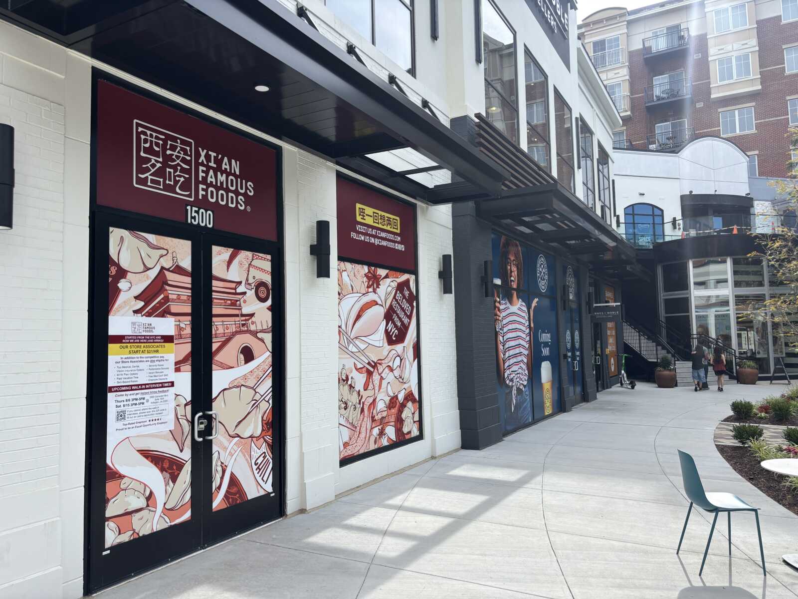 Exterior view of a row of restaurant storefronts in a shopping plaza, including Xi’an Famous Foods with red signage and illustrated window panels