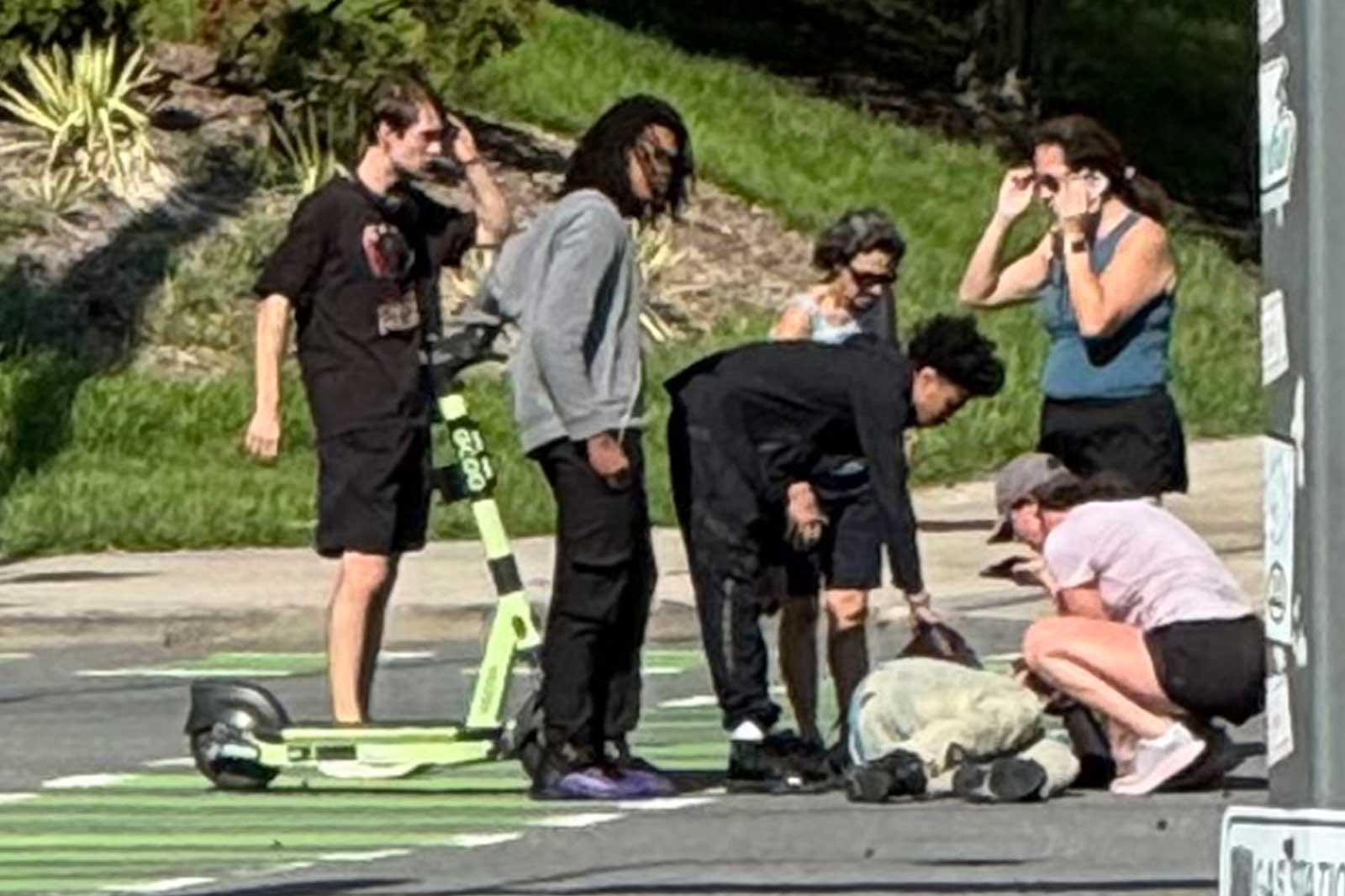 Group of young people crouching and looking at something on the pavement near a lime-green kick scooter.