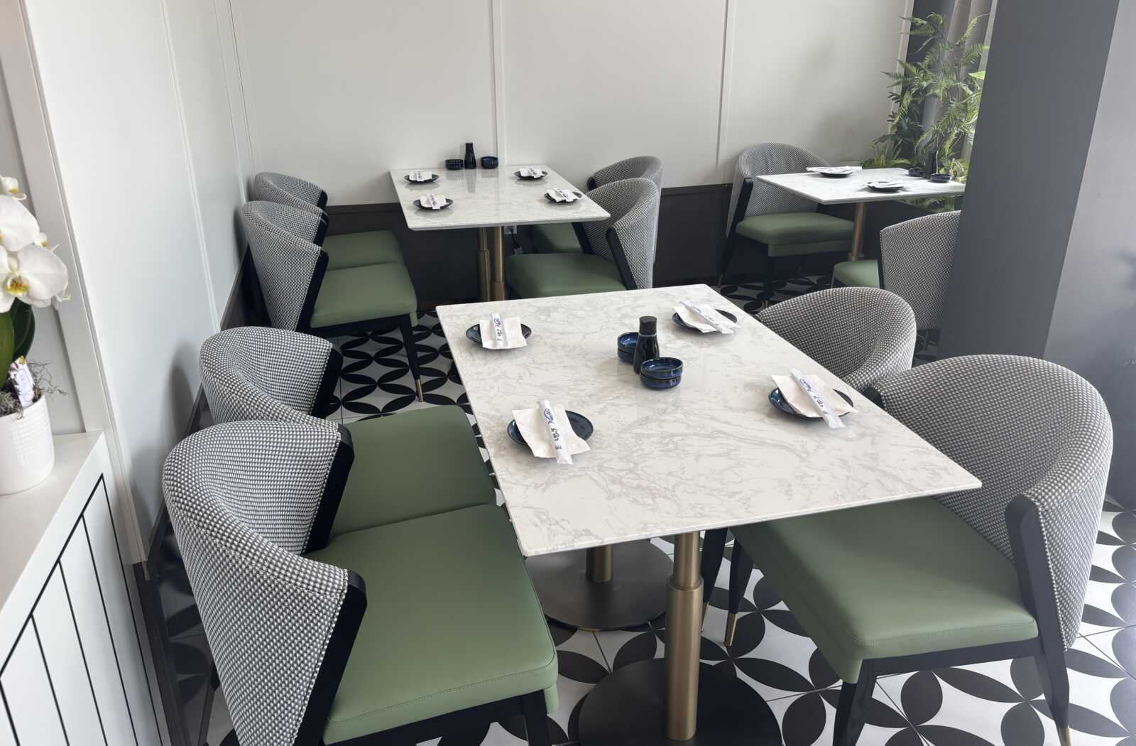 Cafe seating area with marble tabletops, green cushioned chairs, and a black-and-white geometric floor pattern.