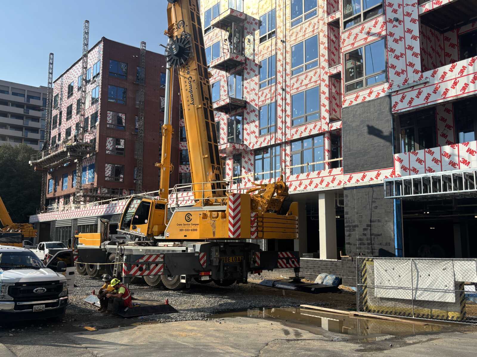 Large yellow crane at a construction site beside a multi-story building under renovation with wrap-covered exterior.