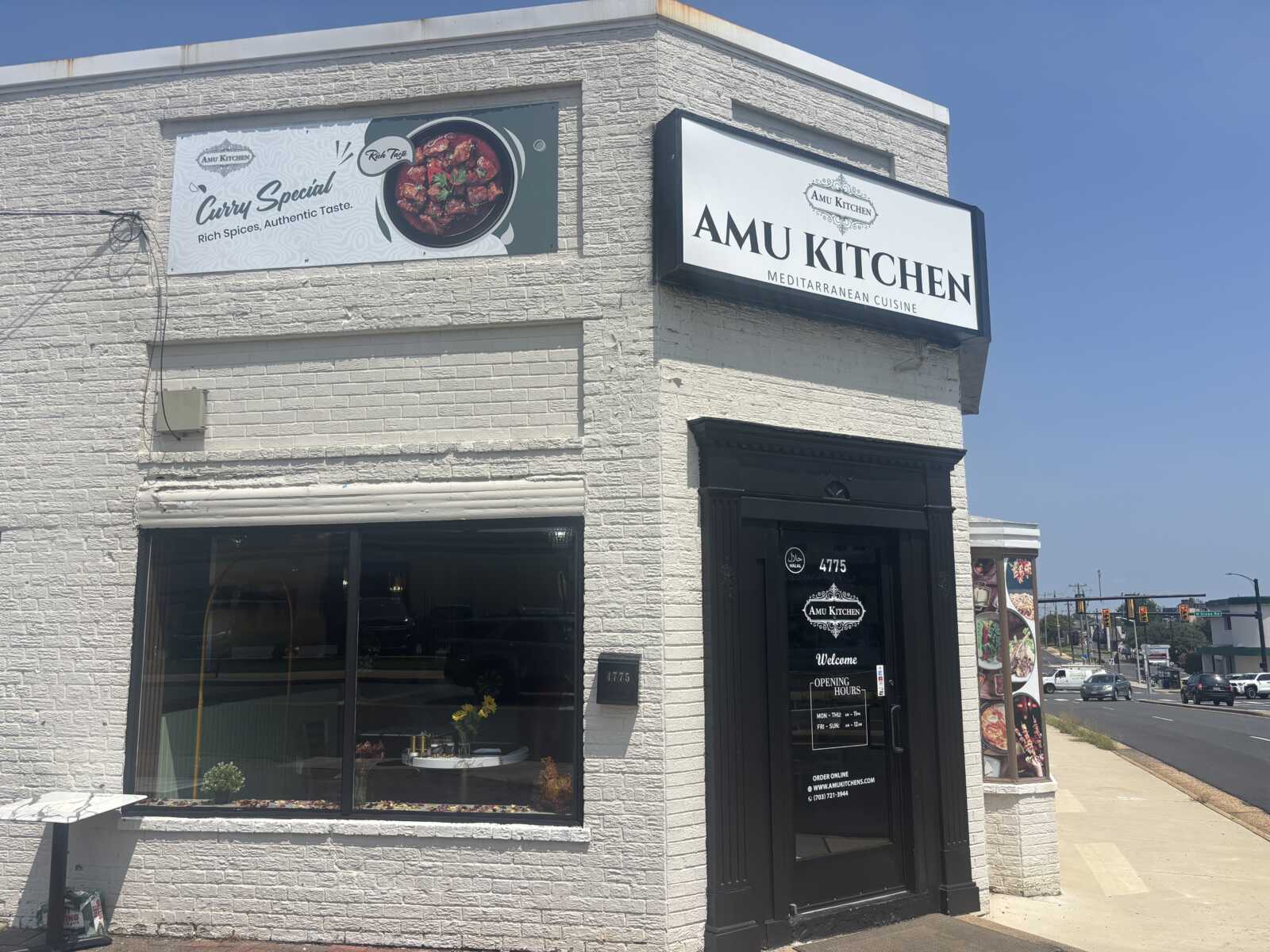 White brick corner restaurant with black doorway, sign reading AMU KITCHEN Mediterranean Cuisine, and a banner advertising Curry Special on the left.