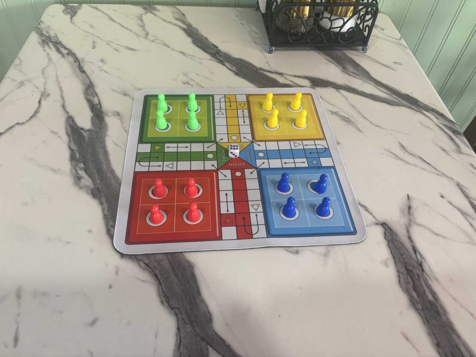 Ludo game board on a marble table with red, blue, green and yellow pawns in their starting areas.
