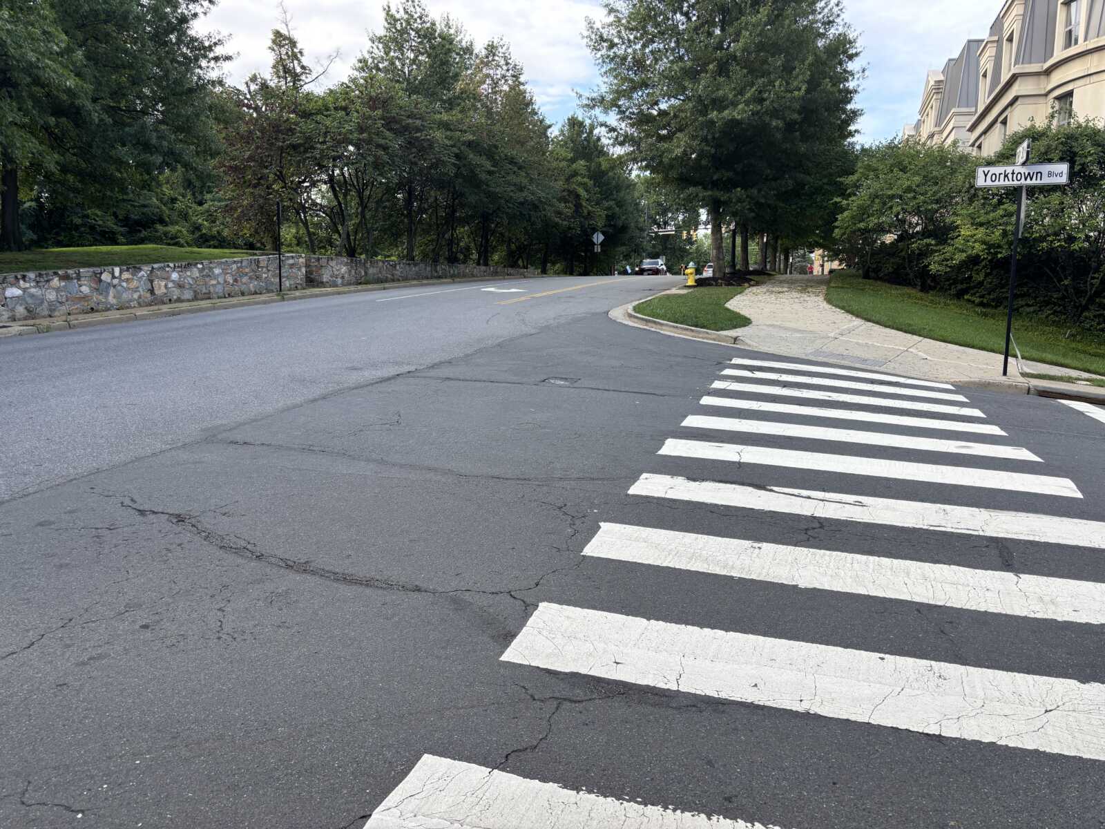 Crosswalk across a quiet residential street with white striped crosswalk and Yorktown Blvd sign visible, trees and side sidewalk in the background.
