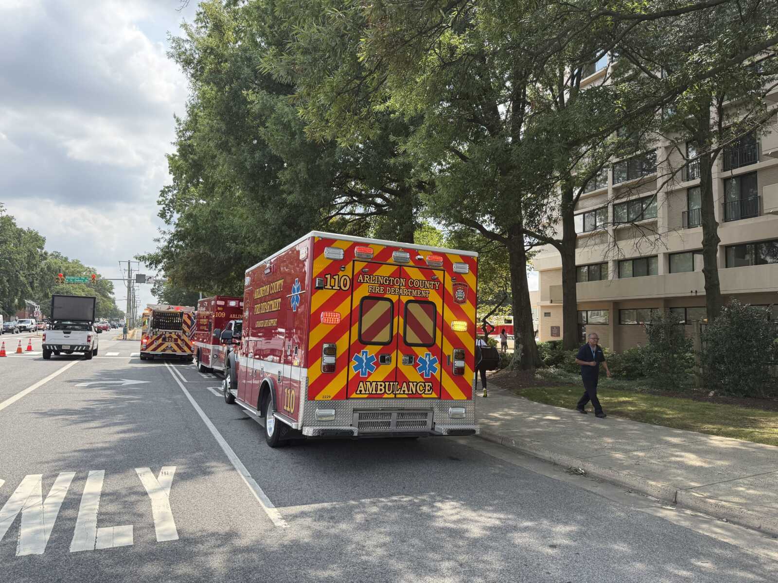 Rear view of a bright red ambulance with yellow chevron stripes parked on a city street; Arlington County Fire Department on the rear doors visible.