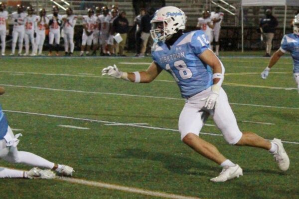 Yorktown football player in light blue jersey #18 runs downfield during a game on a turf field.