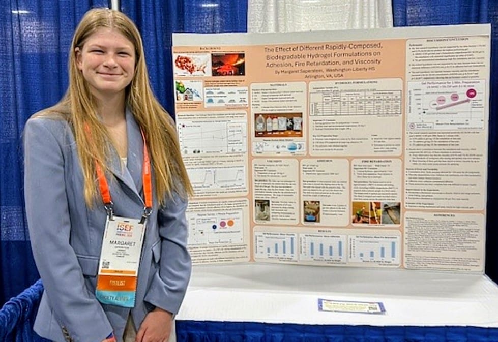 Margaret Saperstein earned top honors at the Regeneron International Science Fair (photo courtesy APS) | ARLnow Young woman in a blue blazer stands beside a large research poster at a conference venue.