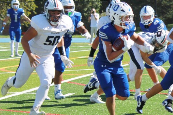 Blue jersey ball carrier (#7) runs with the ball while a white-uniform defender (#50) pursues on a green turf field.