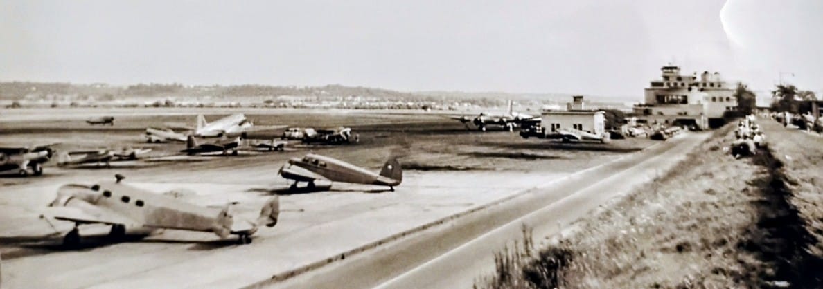 Old airfield with small propeller airplanes parked on the tarmac, mid-20th century.