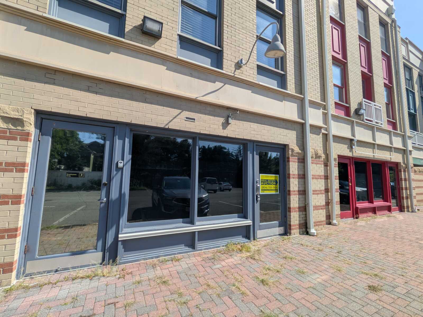Storefront with large glass doors and windows in a beige brick building; a yellow auction sign in the door window on the right side.