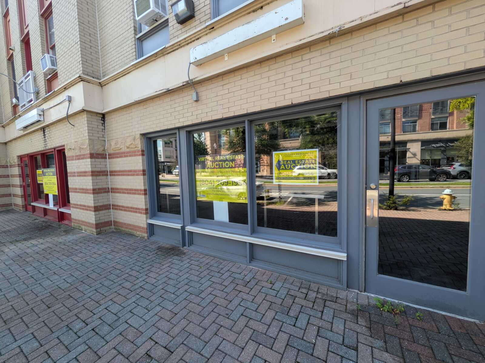 Brick storefront with gray-framed windows and yellow 'Auction' signs in the display windows.