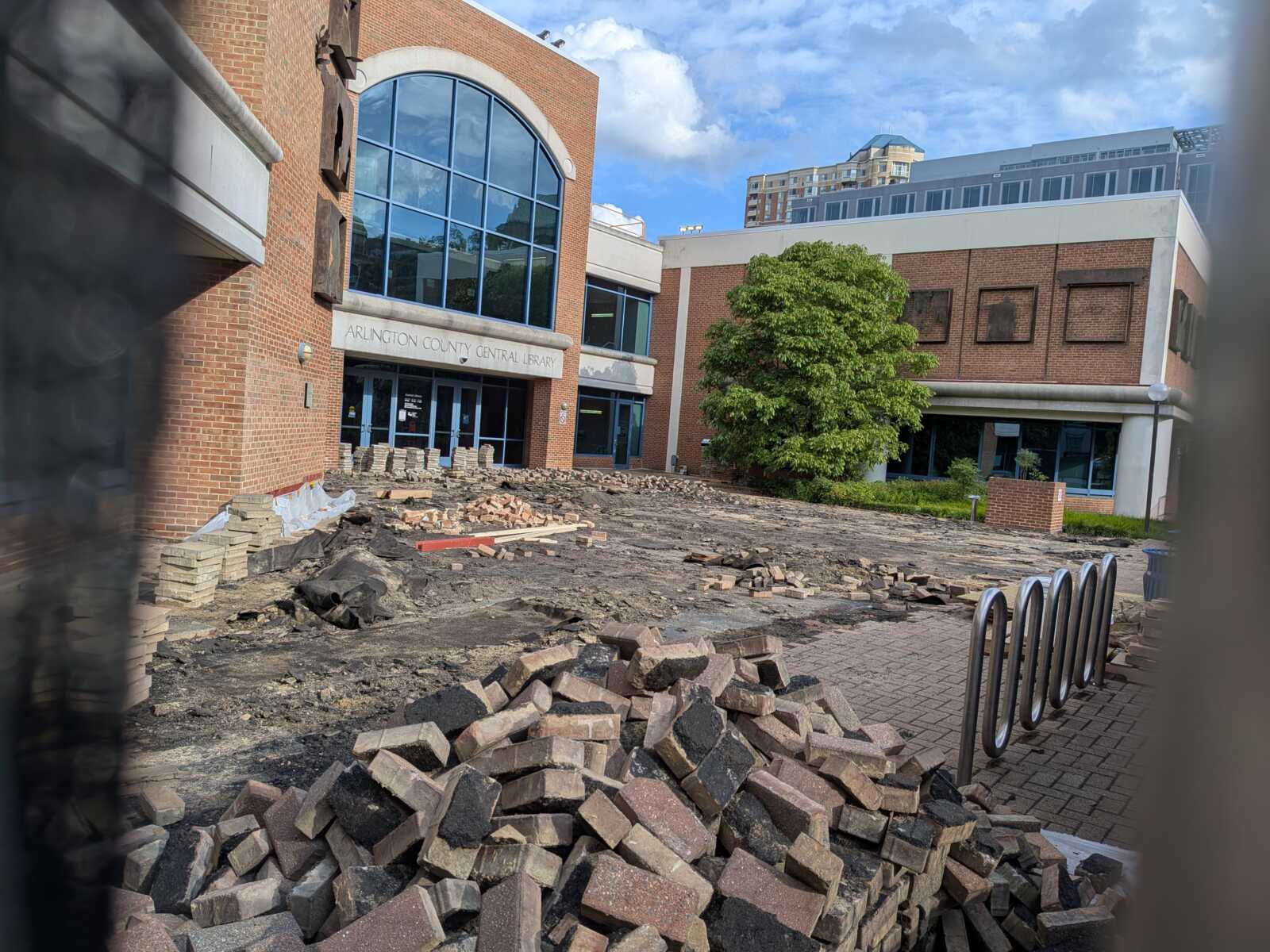 Construction debris and bricks pile up in front of Arlington County Central Library during renovation, with a large arched windowed entrance behind.