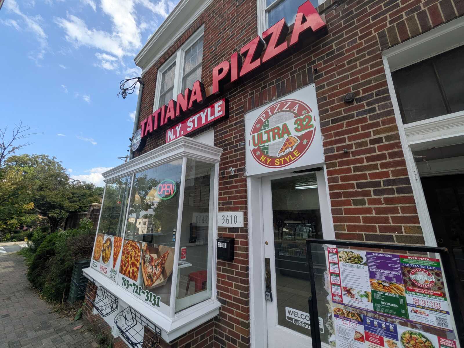 Brick storefront of Tatiana Pizza with large red NY Style sign and a circular Ultra 32 pizza sign beside the door.